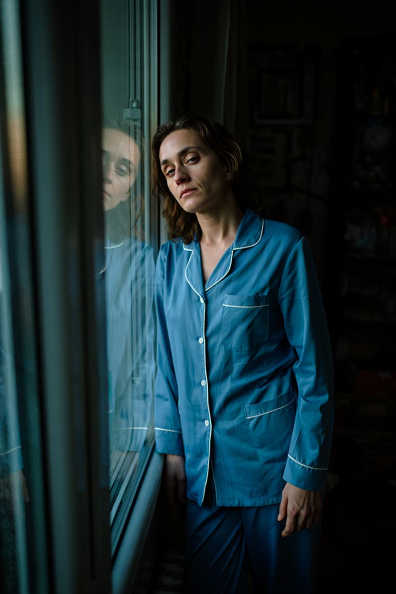 Женщина стоит в пижаме и смотрит в окно